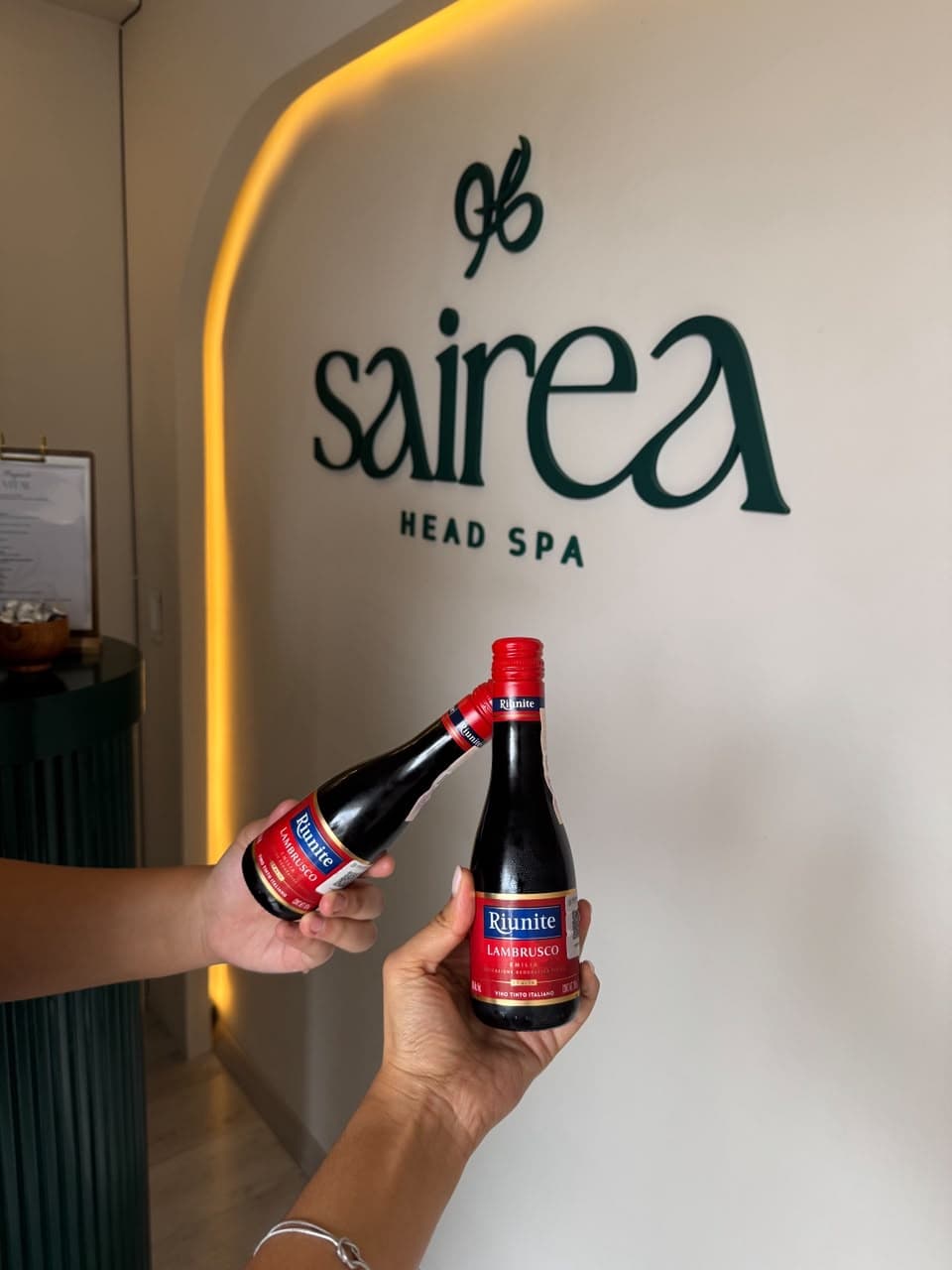 Botellas de vino tinto Lambrusco frente al logo de Sairea Head Spa